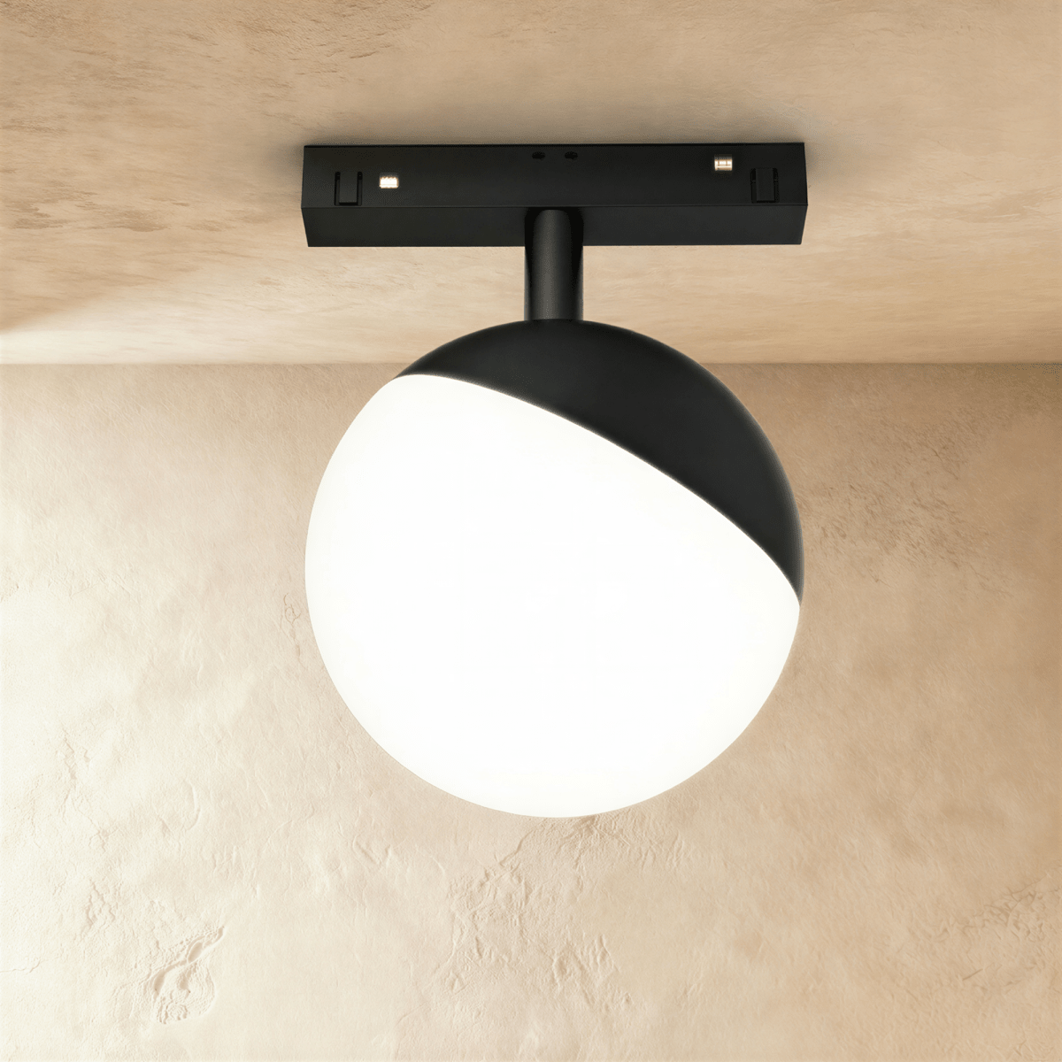 Clérachic black and white globe track lamp mounted close to the ceiling rail without a hanging cord, lit warmly.