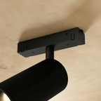 Clérachic detail of a track spotlight's ceiling canopy and swivel joint, shown in matte black metal from below.