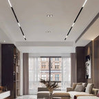 Clérachic linear track lighting and spotlight heads installed along a living room ceiling above a curtained window.