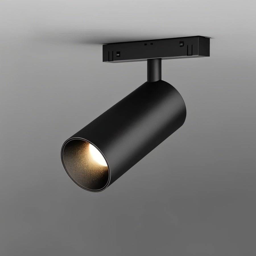 Clérachic matte black cylindrical track spotlight photographed close against grey, its warm beam just visible.