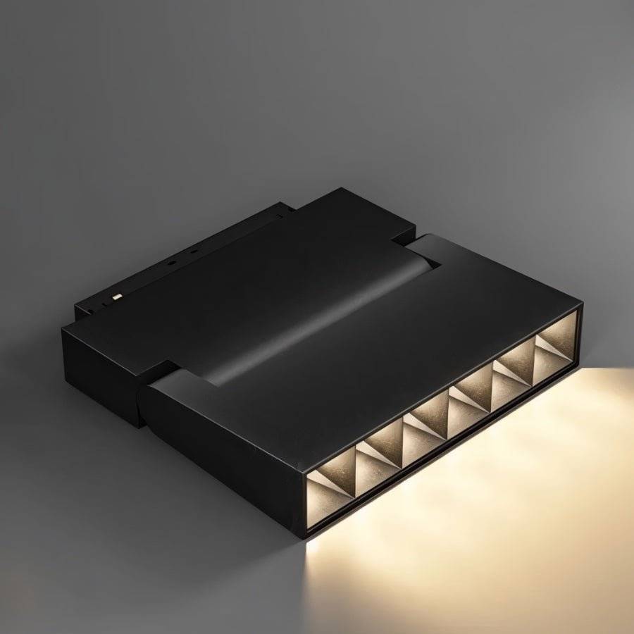Clérachic black linear grille spotlight tilted to show its pyramid-lens cells glowing warm against a grey ground.