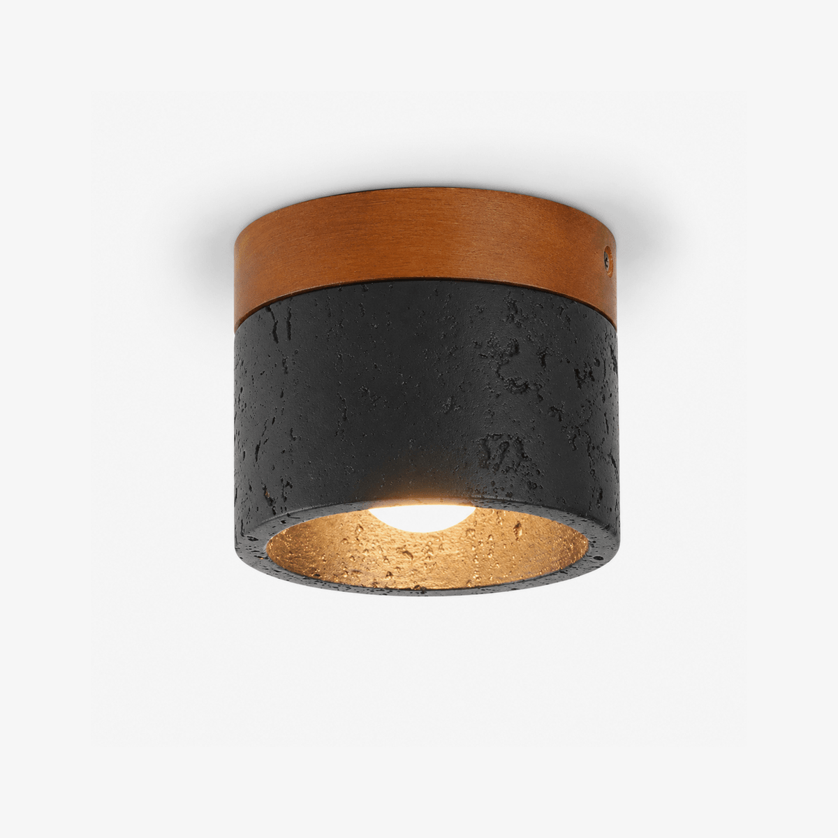 This Clérachic flush-mount ceiling light on white, a black porous travertine cylinder under a walnut-brown top plate, a bulb glowing inside.