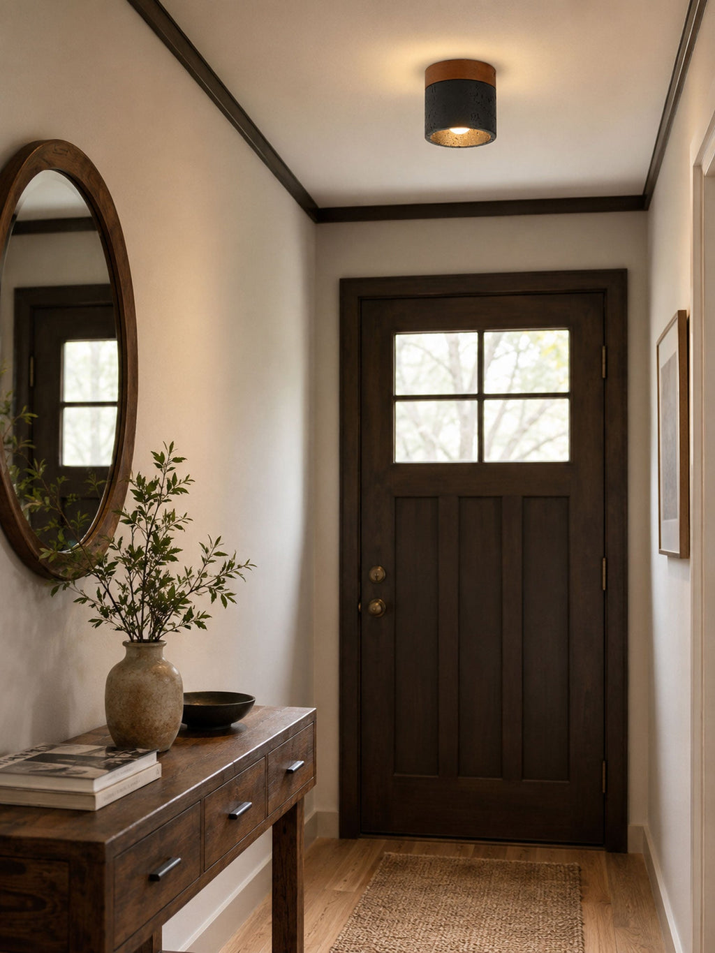 In an entrance hall with a dark front door, a round mirror and a console table, a Clérachic flush ceiling light glows above.