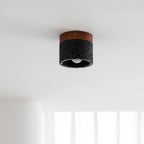Seen from below on a white ceiling, this Clérachic flush ceiling light shows its walnut plate, black stone body and open base.