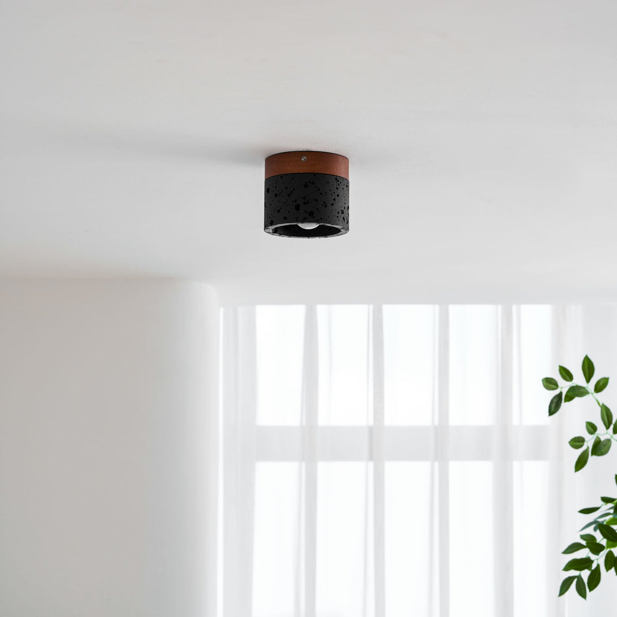 Small on a white ceiling above sheer curtains, a Clérachic flush ceiling light hangs with its walnut top and pitted black body.