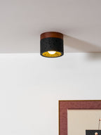 Warm gold glows inside the black stone cylinder of this Clérachic flush ceiling light, a framed print on the wall below.