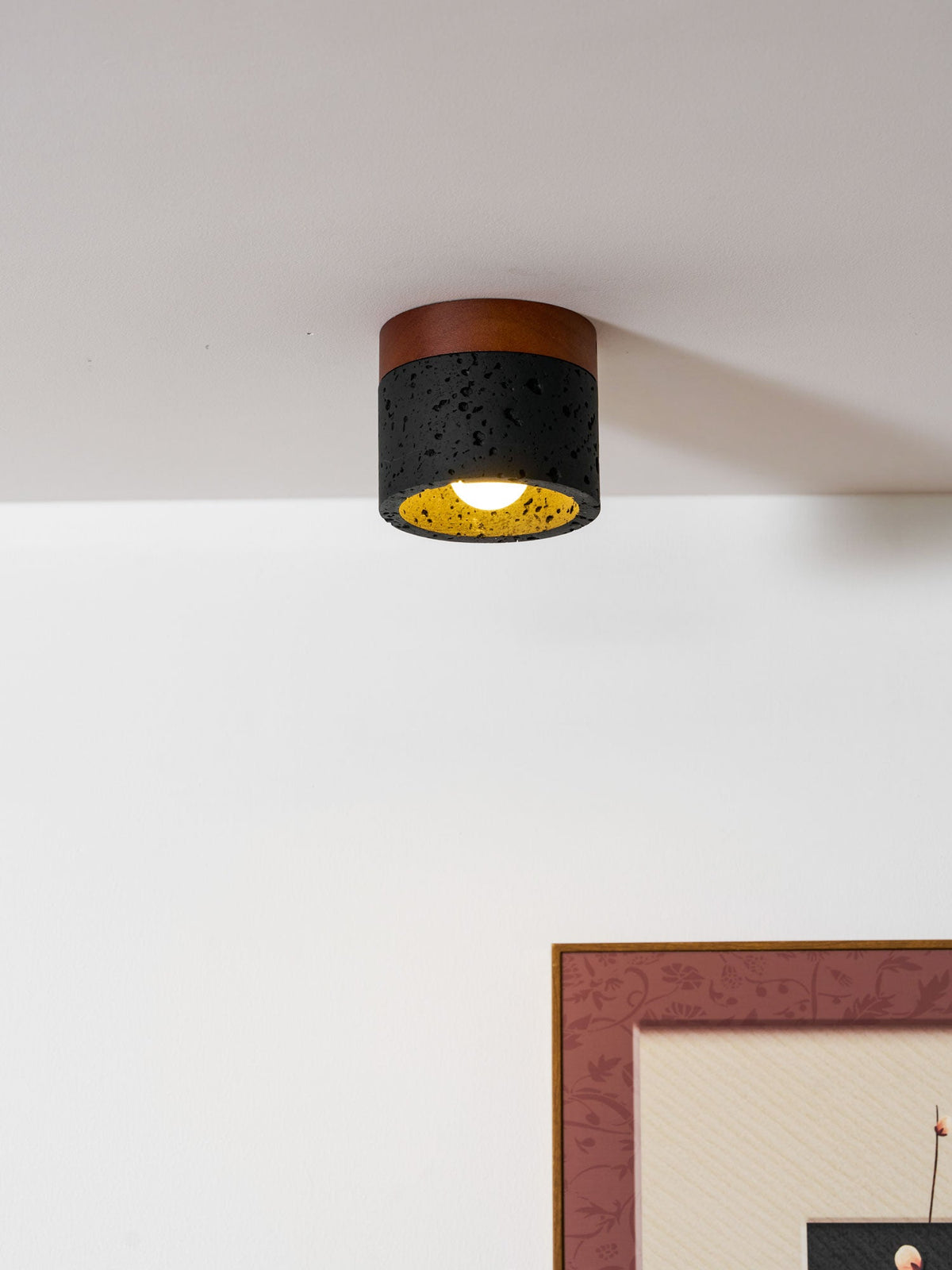 Warm gold glows inside the black stone cylinder of this Clérachic flush ceiling light, a framed print on the wall below.
