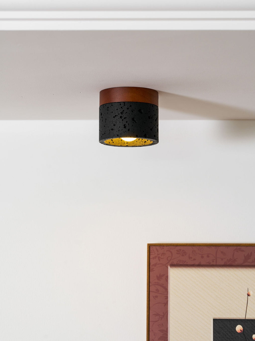 Lit Clérachic flush ceiling light with a golden inner lining, mounted at a white ceiling corner above a framed print.