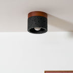 Close view of a Clérachic flush ceiling light under a white ceiling, its black pitted travertine and bare bulb in focus.