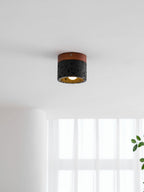 A lit Clérachic flush ceiling light seen from a low angle, with sheer curtains and a green leaf at the lower edge.