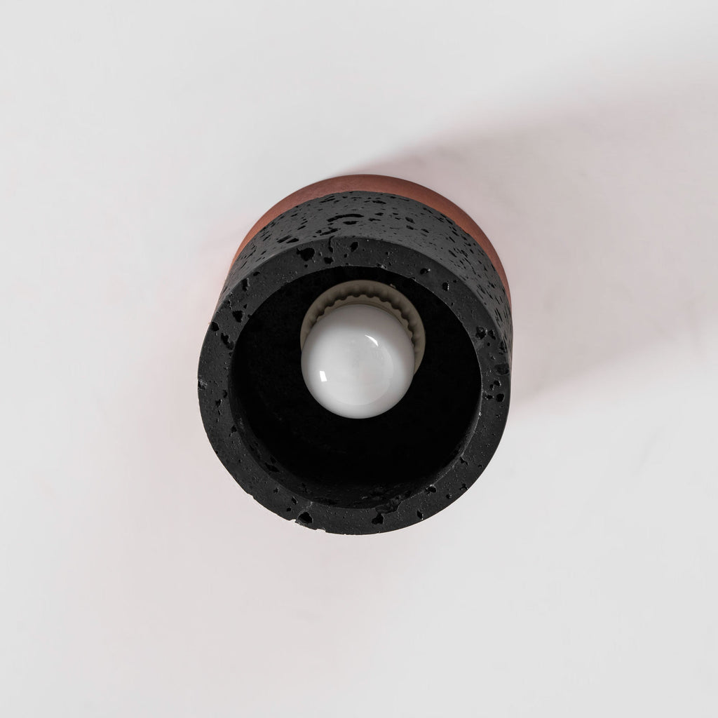 Looking up at the open base of a Clérachic flush ceiling light, with a round white bulb inside a dark, porous stone ring.