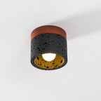 Straight-on view of this Clérachic flush ceiling light, with its walnut plate, black stone cylinder and bulb lit warm.