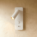 A white wall-mounted reading light with an adjustable spot and USB port glows warm against a plaster wall, Clérachic hero shot.