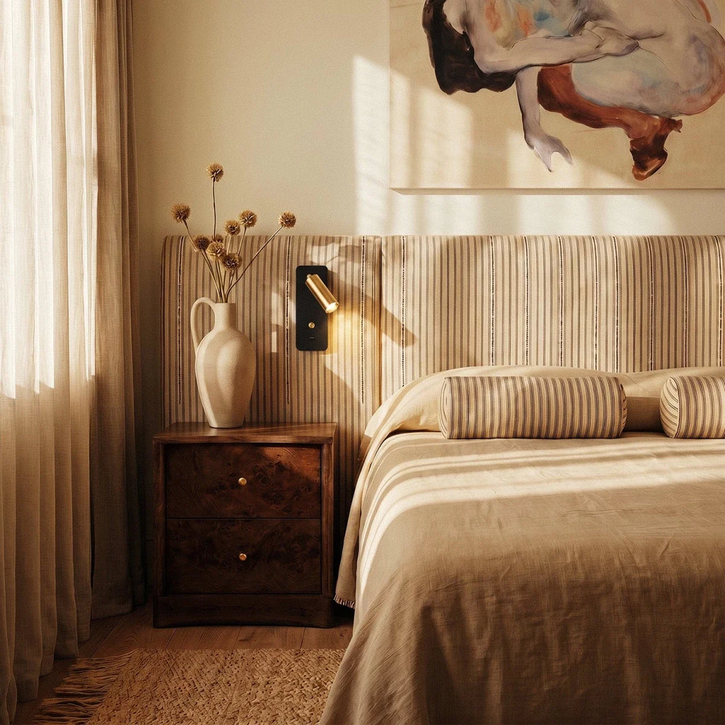The brass-and-black reading light hangs bedside on a striped headboard beneath a figurative painting, Clérachic lifestyle shot.