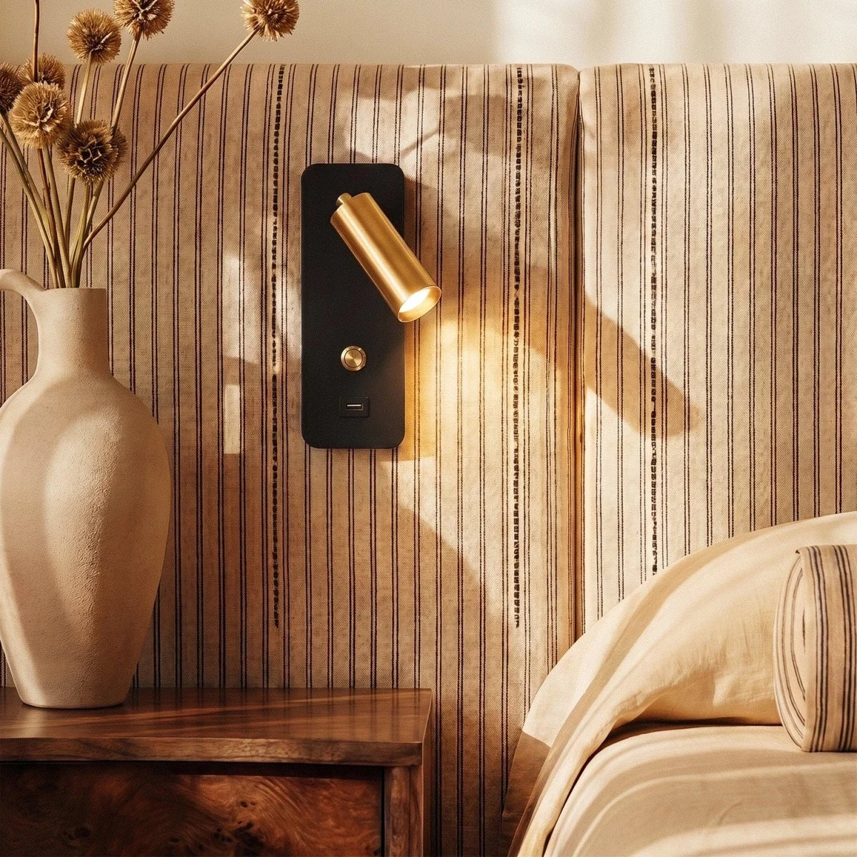 A closer crop shows the brass-and-black reading light glowing beside a stoneware jug of dried flowers, Clérachic lifestyle shot.