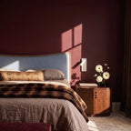 A white reading light hangs unlit above a walnut nightstand in a deep burgundy bedroom with a faux-fur throw, Clérachic lifestyle shot.