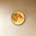 Clérachic illuminated moon wall lamp in warm amber tones, the lunar surface art lit against a plaster wall.