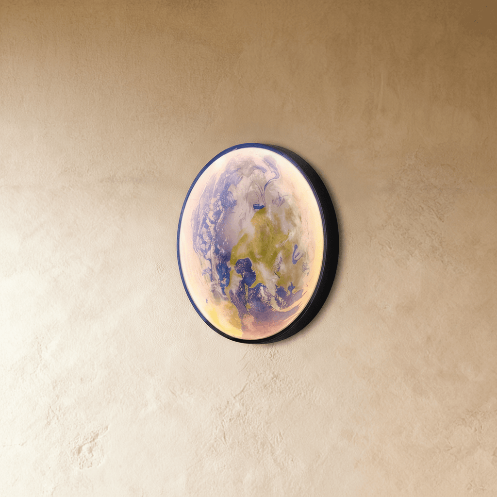 Clérachic illuminated Earth wall lamp glowing softly in blue and green, mounted at an angle on a plaster wall.