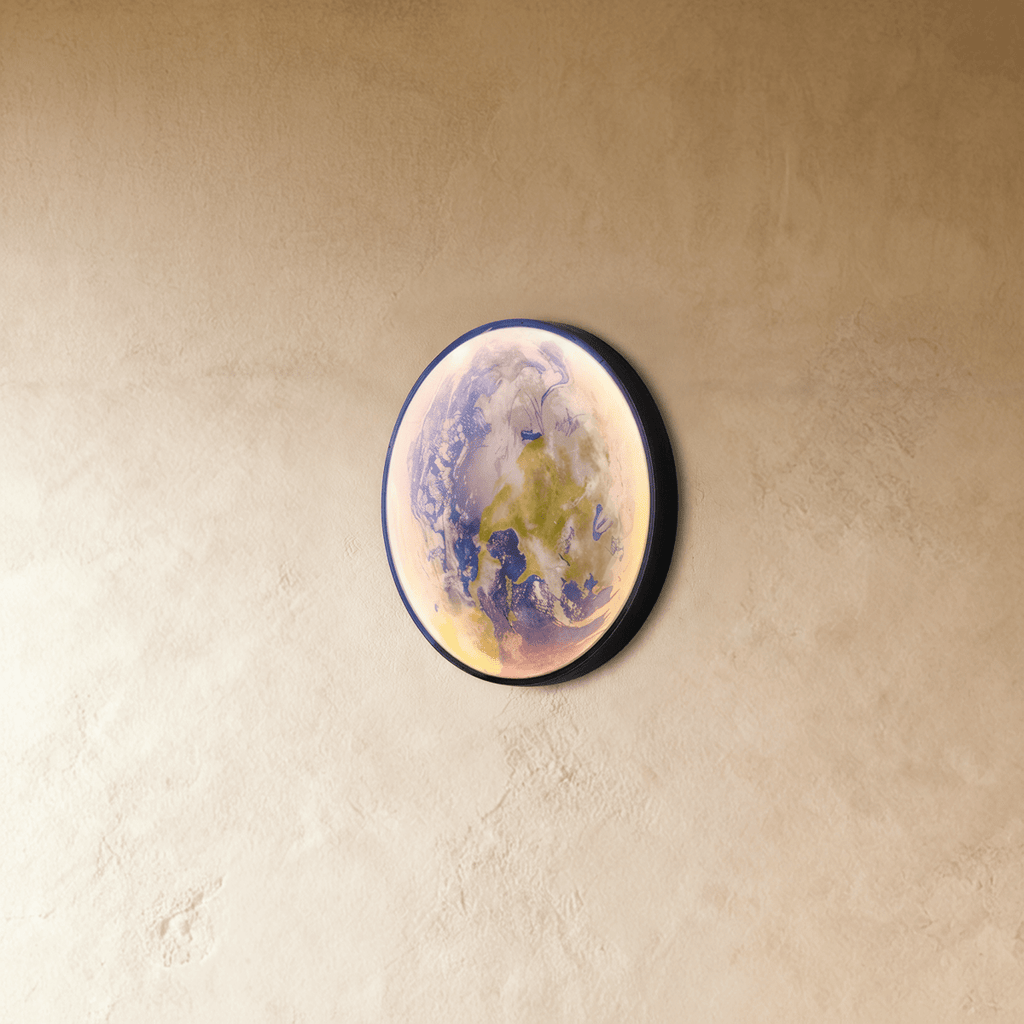 Clérachic illuminated Earth wall lamp glowing in soft blue and green, viewed from a side angle against plaster.