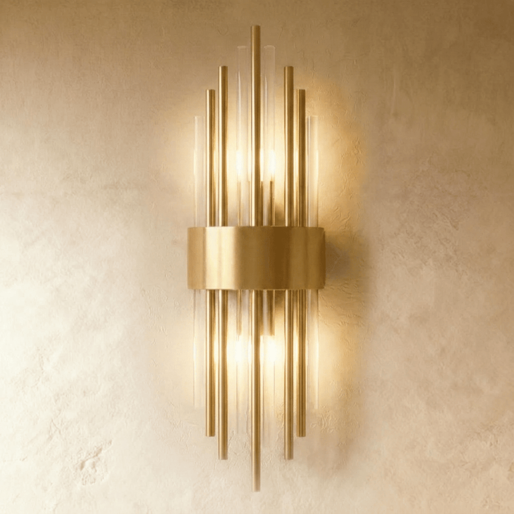 Clérachic brass wall sconce with tall fluted glass rods fanning from a curved gold-tone backplate on a plaster wall.