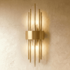 Clérachic brass wall sconce with tall fluted glass rods fanning from a curved gold-tone backplate on a plaster wall.