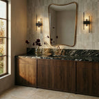 Clérachic black metal wall sconces flanking a gold-framed mirror above a dark marble bathroom vanity.