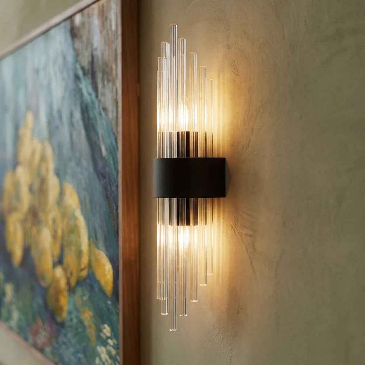 Clérachic black metal wall sconce with fluted glass rods glowing beside a framed still-life painting.