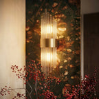 Clérachic brass wall sconce with fluted glass rods glowing against a dark floral wall, framed by red berry stems.