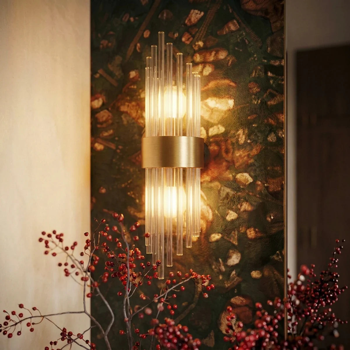 Clérachic brass wall sconce with fluted glass rods glowing against a dark floral wall, framed by red berry stems.