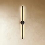 Clérachic black slim wall light glows along its full length, round canopy centred on a warm plaster wall.