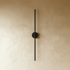 Clérachic black slim wall light shown unlit, a thin rod fixed by a round canopy to a plaster wall.