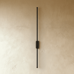 Clérachic black slim wall light shown unlit, a thin rod fixed by an oval canopy to a plaster wall.