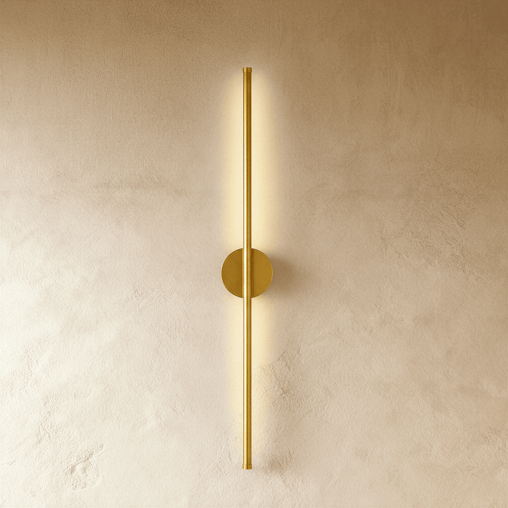 Clérachic brushed gold slim wall light glows along its full length, round canopy on a warm plaster wall.