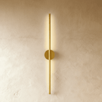 Clérachic brushed gold slim wall light glows along its full length, round canopy on a warm plaster wall.