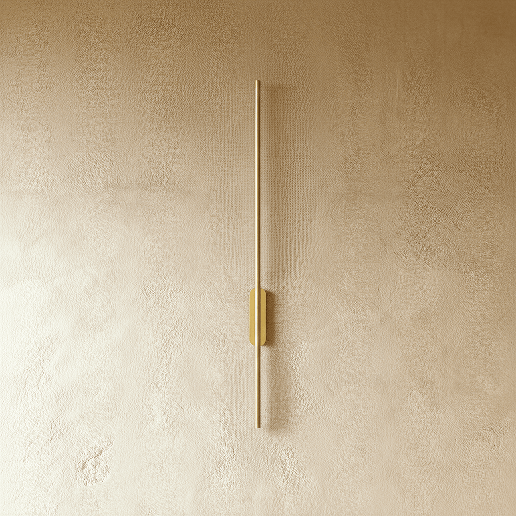 Clérachic brushed gold slim wall light shown unlit, a thin rod fixed by an oval canopy to a plaster wall.