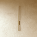 Clérachic brushed gold slim wall light shown unlit, a thin rod fixed by an oval canopy to a plaster wall.