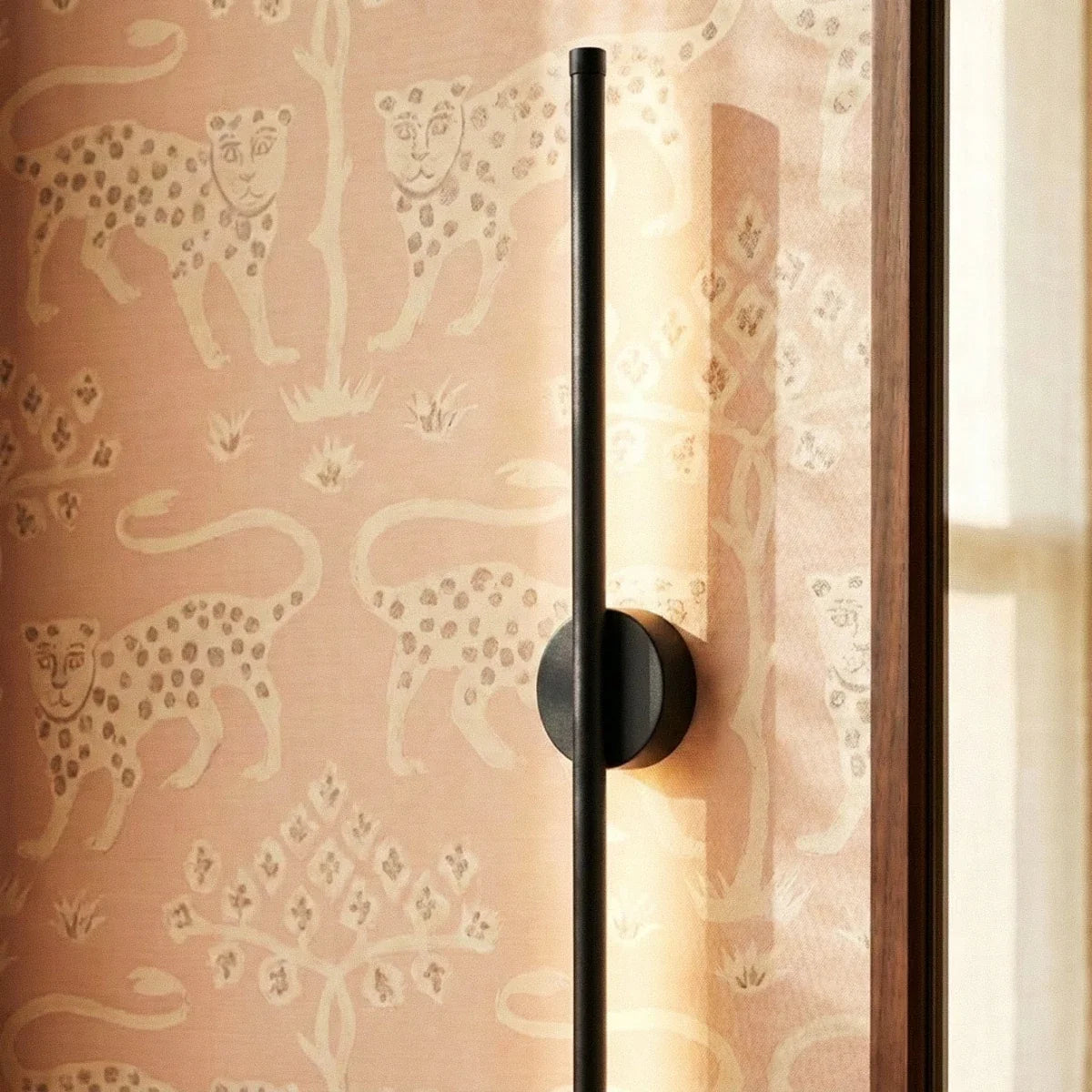 Clérachic close-up of the black slim wall light's round canopy against leopard-print pink wallpaper.