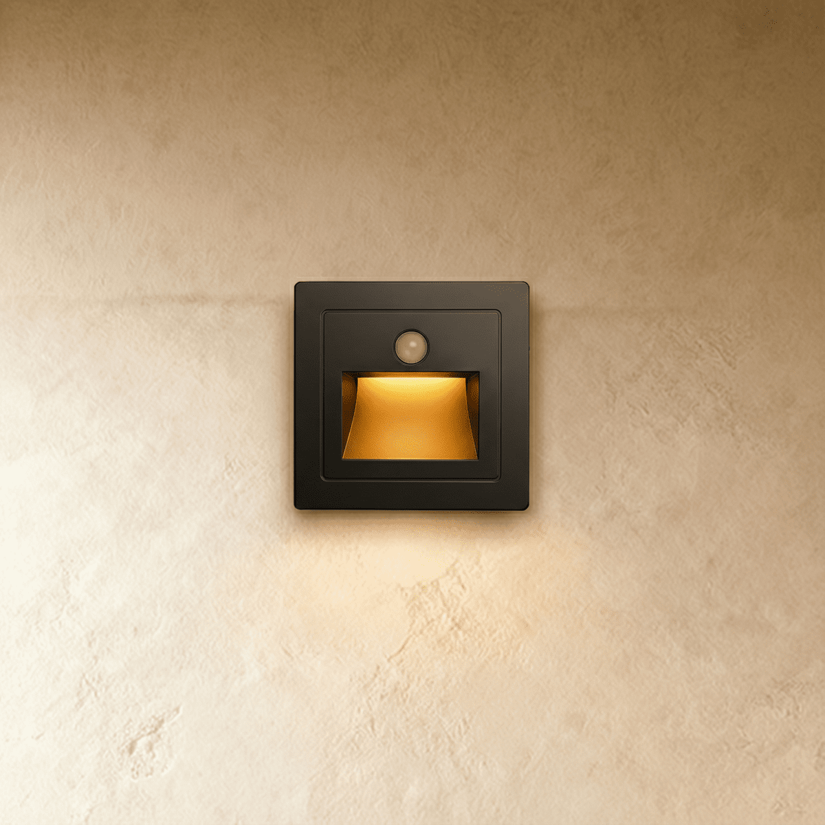 A square black recessed step light casts a warm downward glow from its motion sensor housing on a plaster wall, Clérachic hero shot.