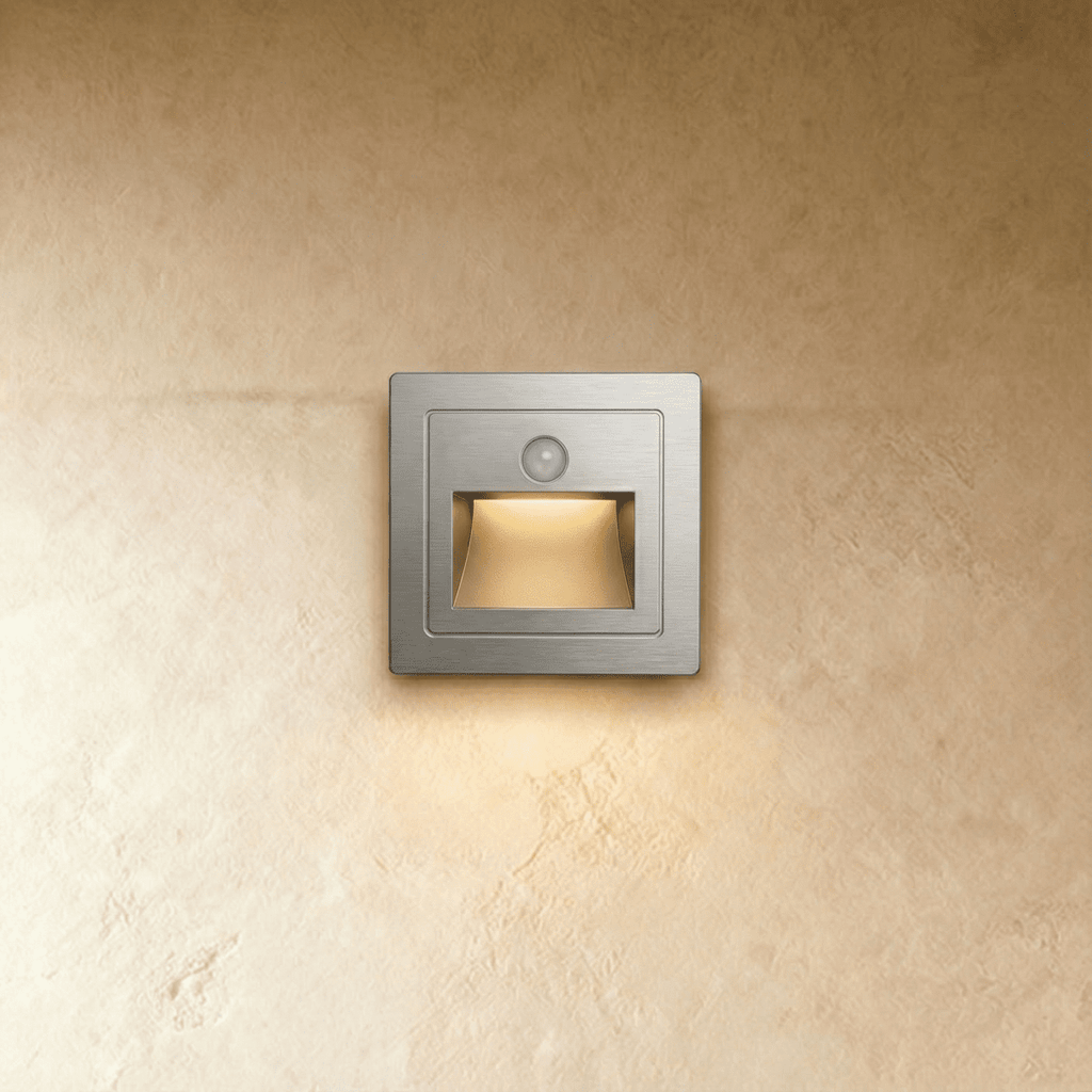 A brushed silver recessed step light glows warm from its trapezoid light chamber against plaster in this Clérachic hero shot.