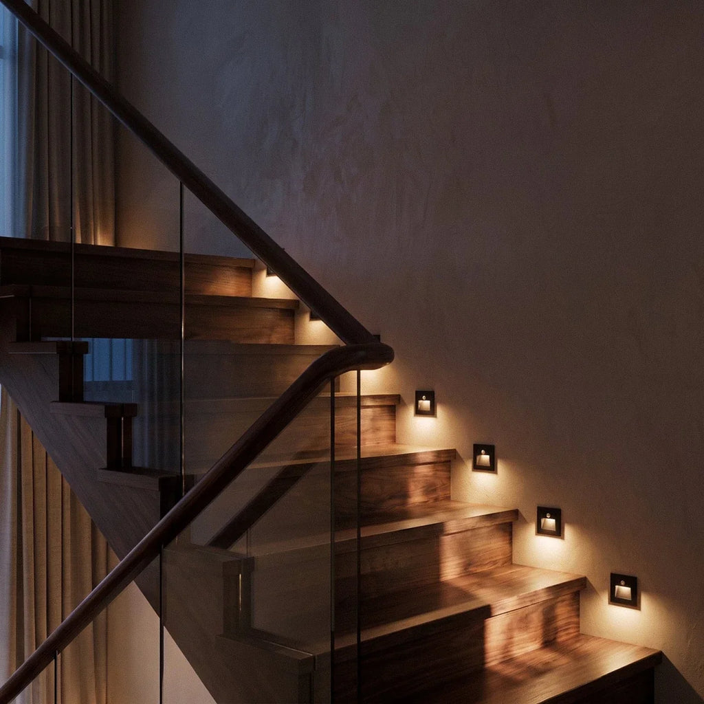 At night, the black recessed step lights glow warm along the same walnut staircase treads, Clérachic lifestyle shot.