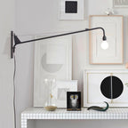 Clérachic black swing-arm wall light above a white tiled shelf, reaching over framed prints and a glass hourglass.