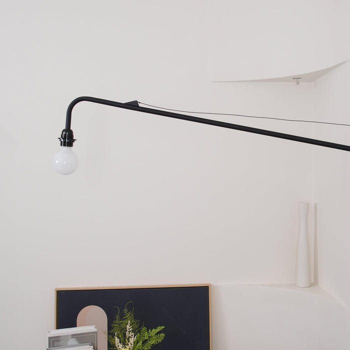 Close view of the black arm, tensioning wire and bulb holder of this Clérachic wall light, with a globe bulb at the tip.