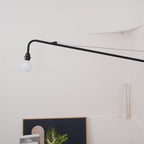 Close view of the black arm, tensioning wire and bulb holder of this Clérachic wall light, with a globe bulb at the tip.