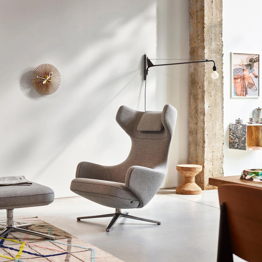 Clérachic swing-arm wall light on a concrete-pillared wall above a grey wing-back armchair and a patterned rug.