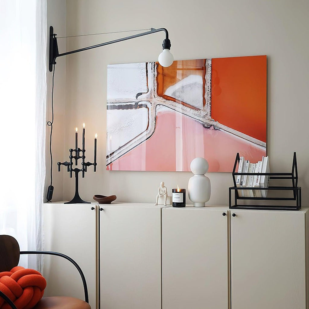 Black swing-arm Clérachic wall light above a white cabinet, with a large orange and pink painting and a candle holder.