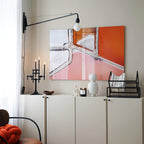 Black swing-arm Clérachic wall light above a white cabinet, with a large orange and pink painting and a candle holder.