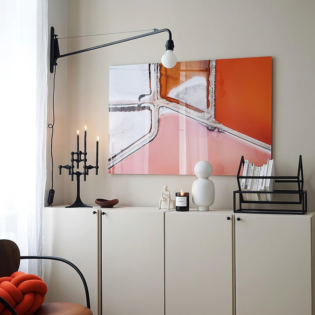 Black swing-arm Clérachic wall light above a white cabinet, with a large orange and pink painting and a candle holder.