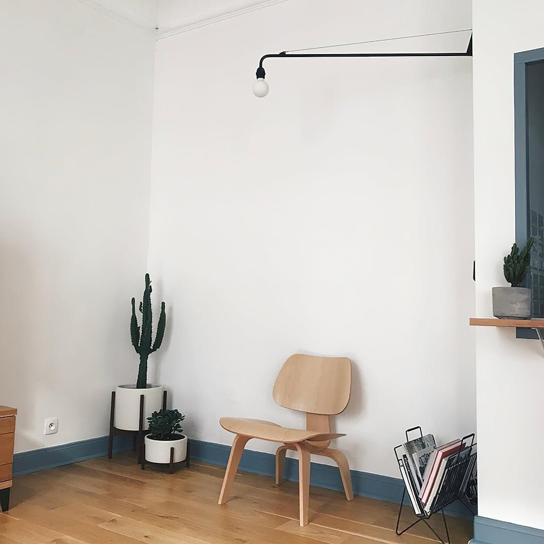 Clérachic swing-arm wall light on a white wall above a plywood chair, a cactus in a white pot and a magazine rack.
