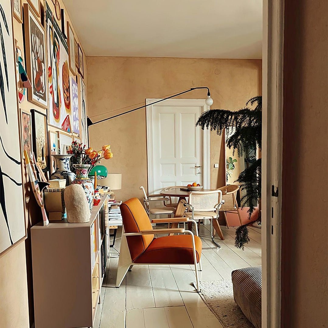 Wide view of a colourful interior with a long black Clérachic swing arm reaching across the wall above an orange chair.
