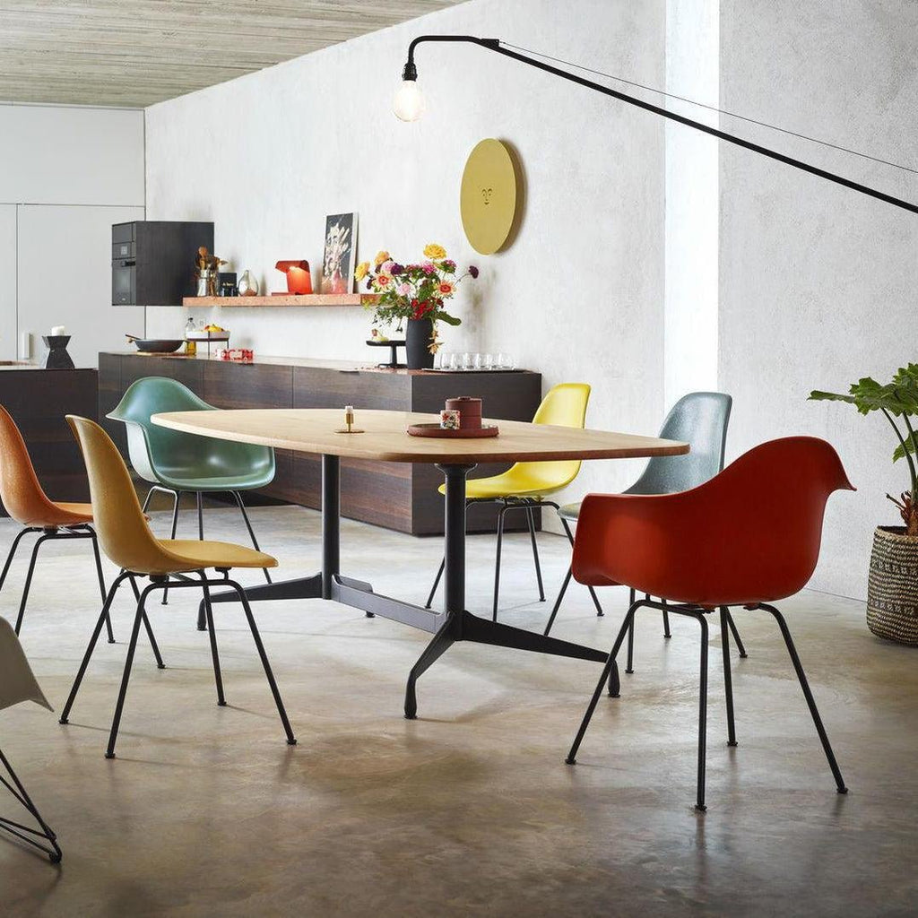 Clérachic swing-arm wall light above a dining area with an oval table, moulded chairs in orange, teal and yellow, and a round clock.
